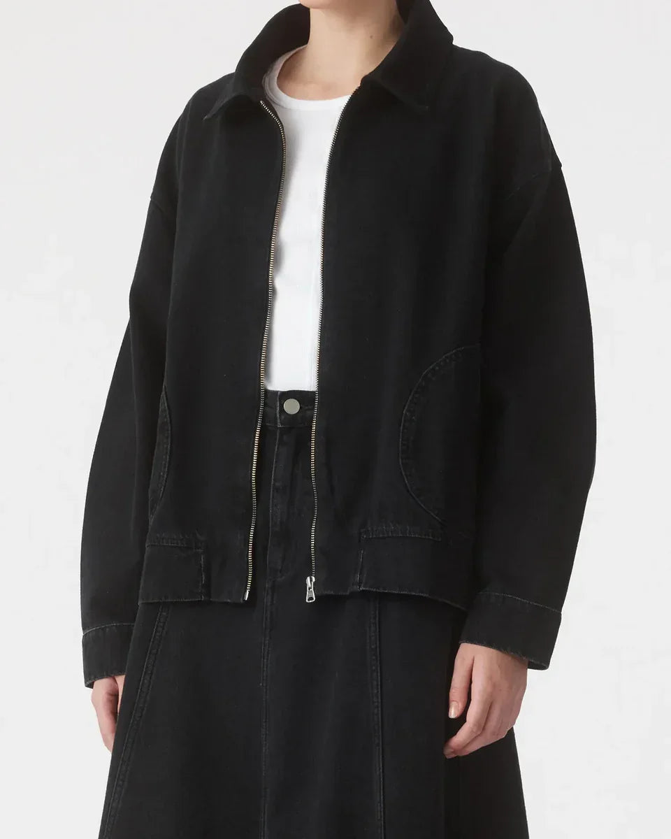 Black zip-front denim jacket with oversized pockets, styled with white tee and black skirt