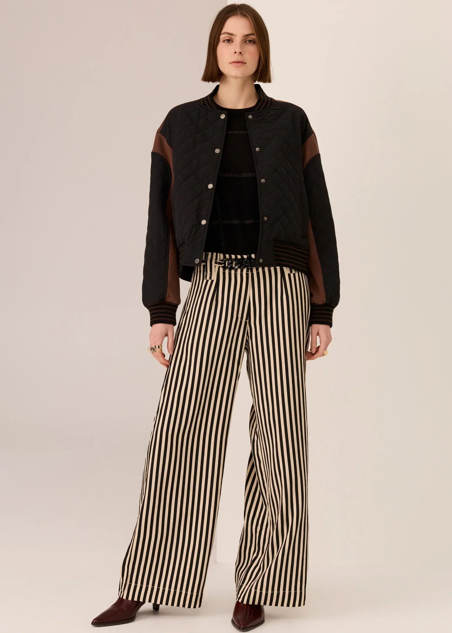 Woman in black quilted bomber jacket, striped wide-leg pants, and burgundy heels for women's fashion