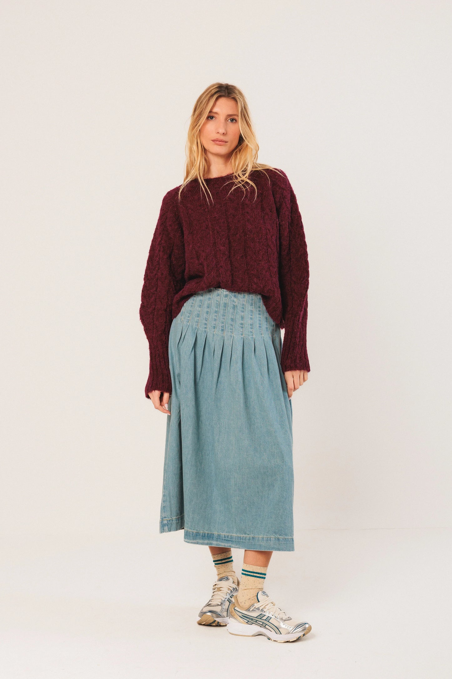Woman in burgundy knit sweater, denim midi skirt, and sneakers for casual chic style