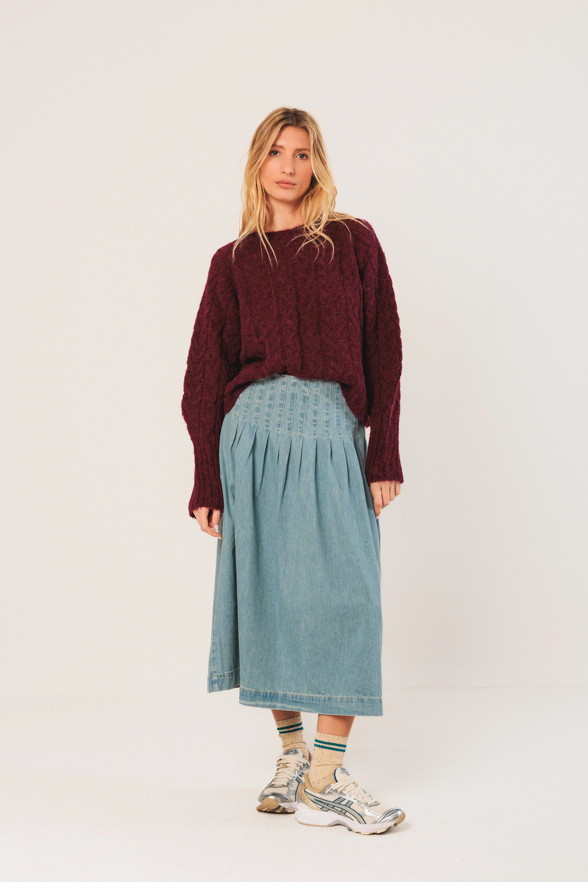 Woman in burgundy knit sweater, denim midi skirt, and sneakers for casual chic style