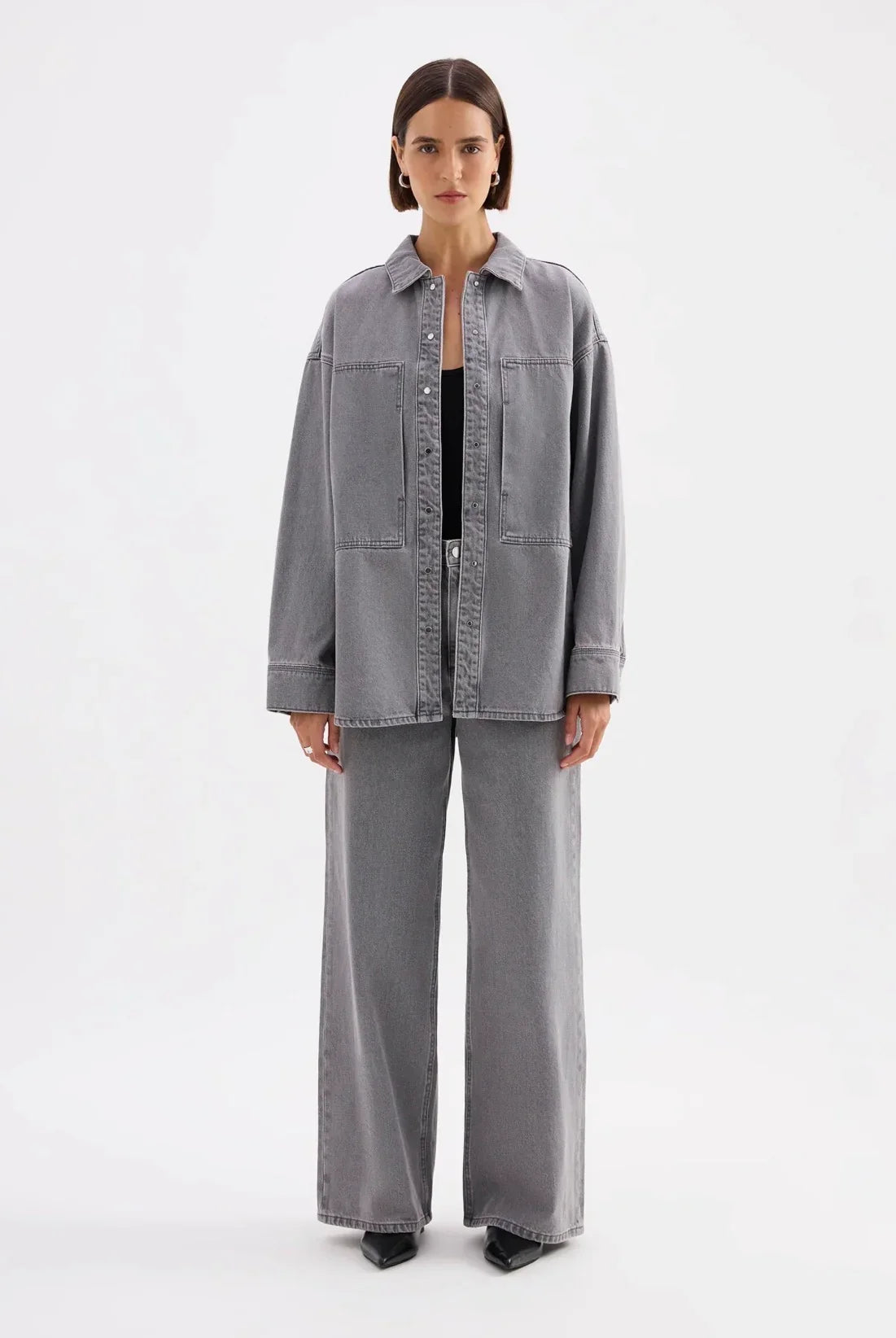 Woman wearing oversized grey denim jacket and wide-leg jeans, minimalist studio background