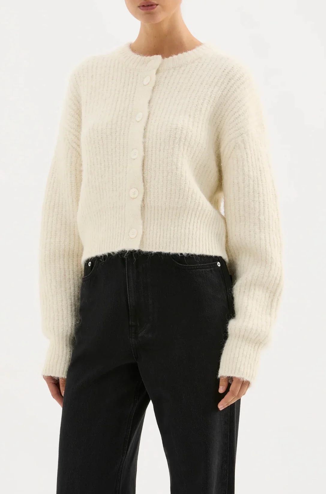 Woman wearing cream knit button-up cardigan and black high-waisted jeans