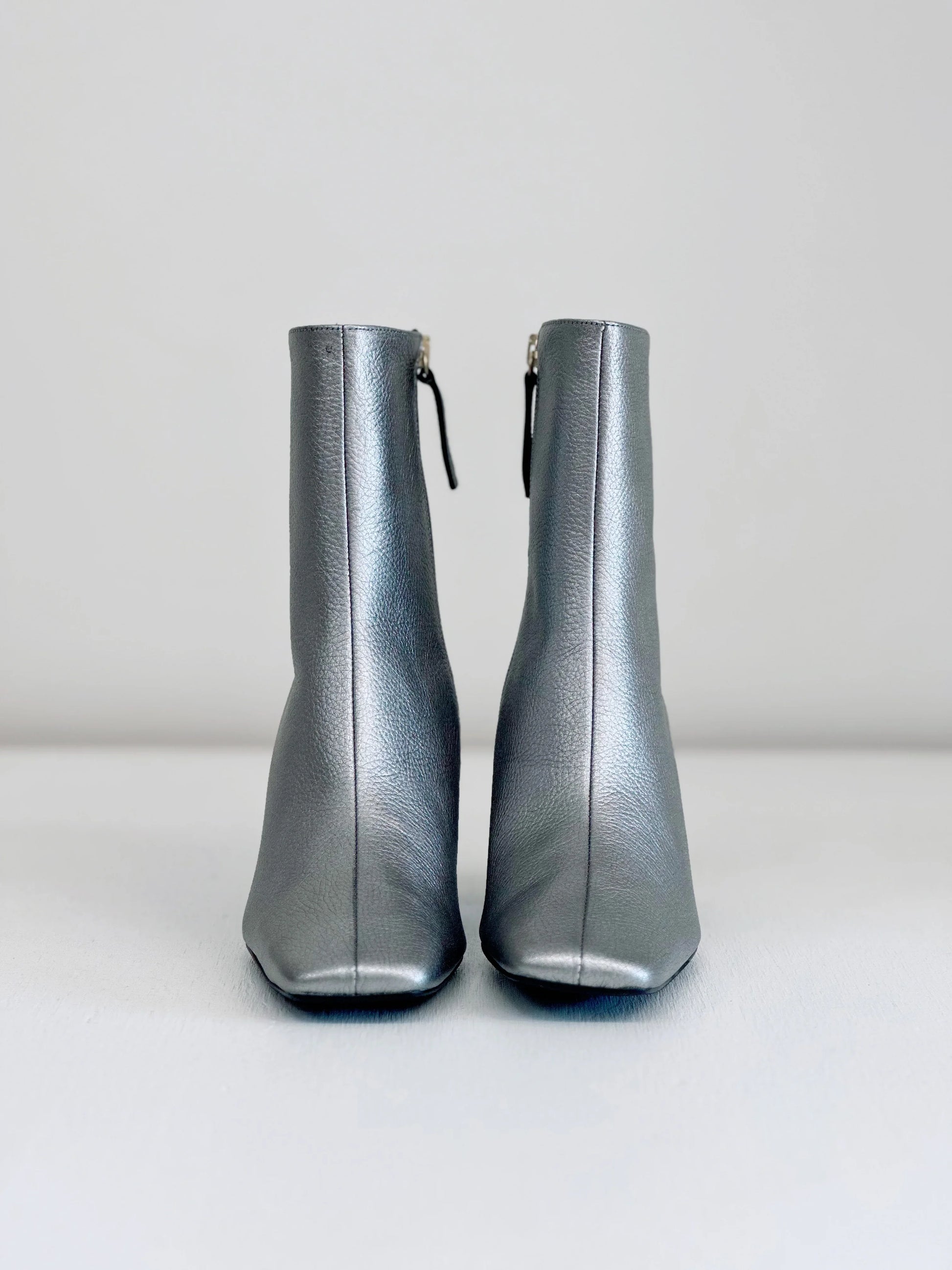 Front view of metallic silver leather ankle boots with zippers on plain background