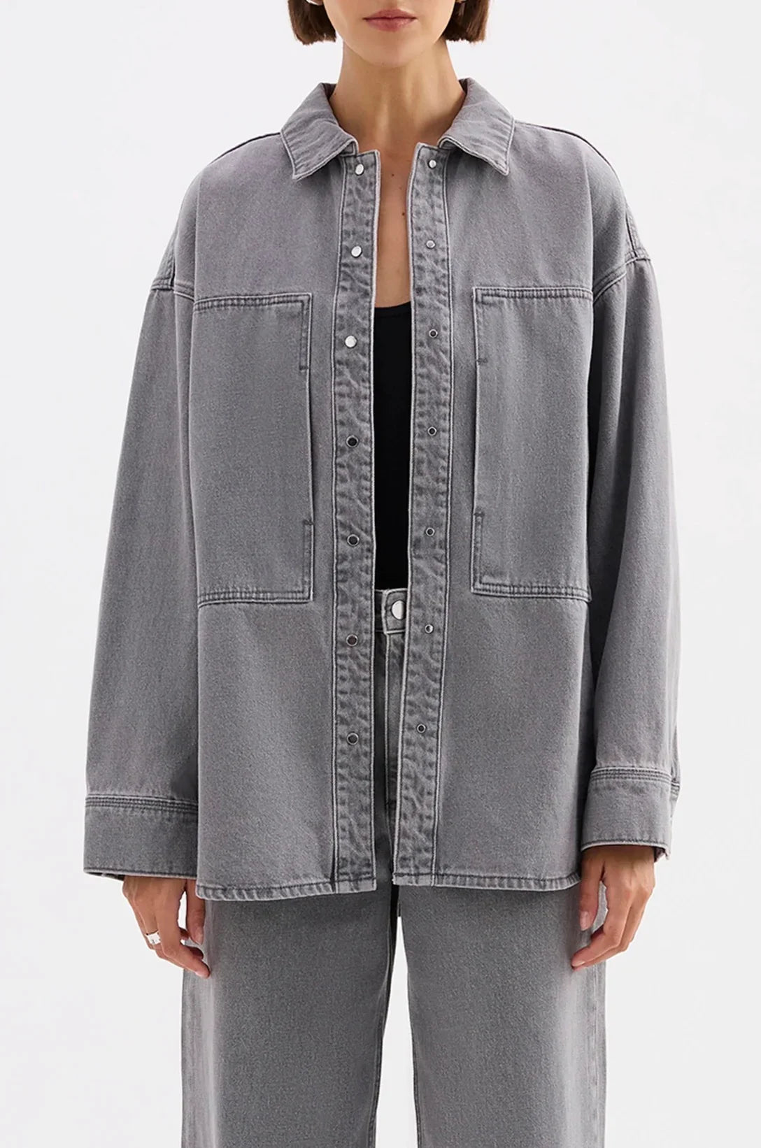 Woman wearing oversized grey denim shirt jacket with front pockets and matching jeans
