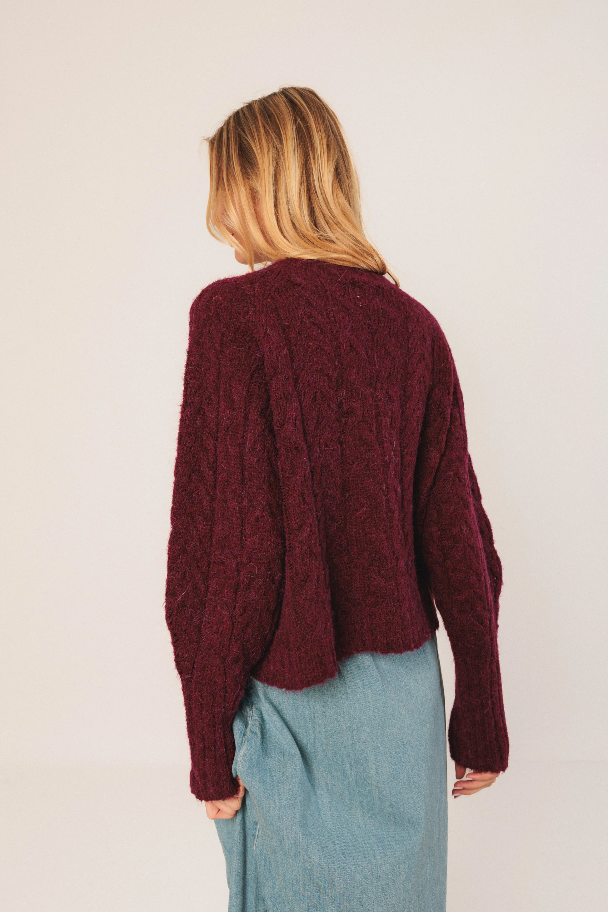 Burgundy cable knit sweater paired with light blue denim skirt, showcasing cozy women's fashion.