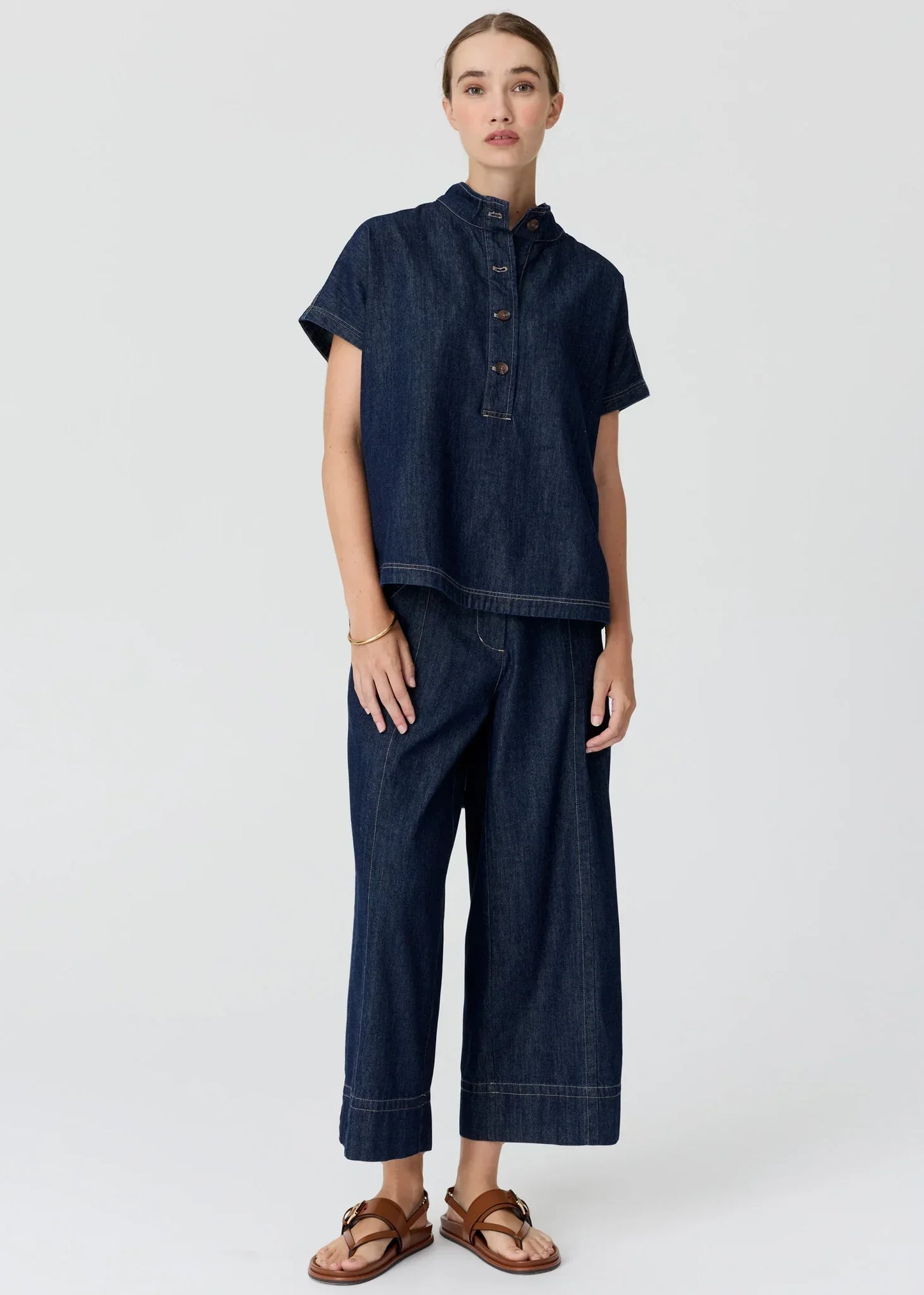 Woman wearing a dark wash denim short sleeve shirt and wide leg trousers with brown sandals