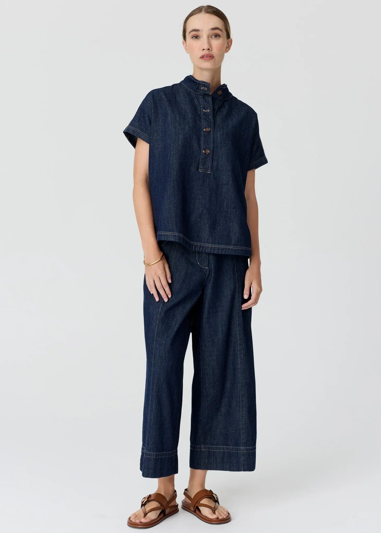 Woman wearing a dark wash denim short sleeve shirt and wide leg trousers with brown sandals