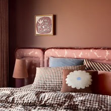 Cozy bedroom with pink velvet headboard, checkered bedding, and floral accent pillow.
