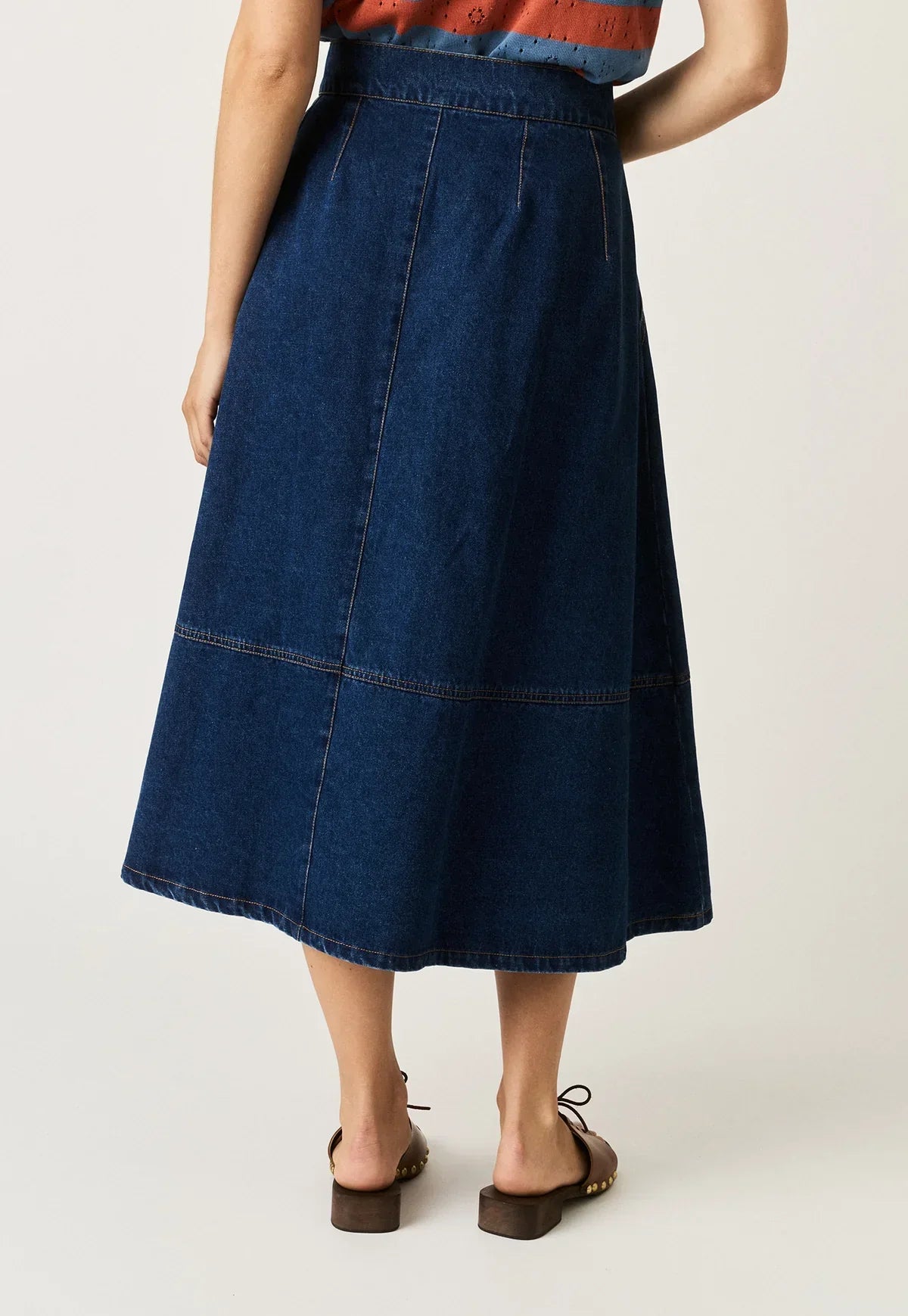 Rear view of the NANCYBIRD Aries Denim Skirt in dark wash paired with brown platform sandals.