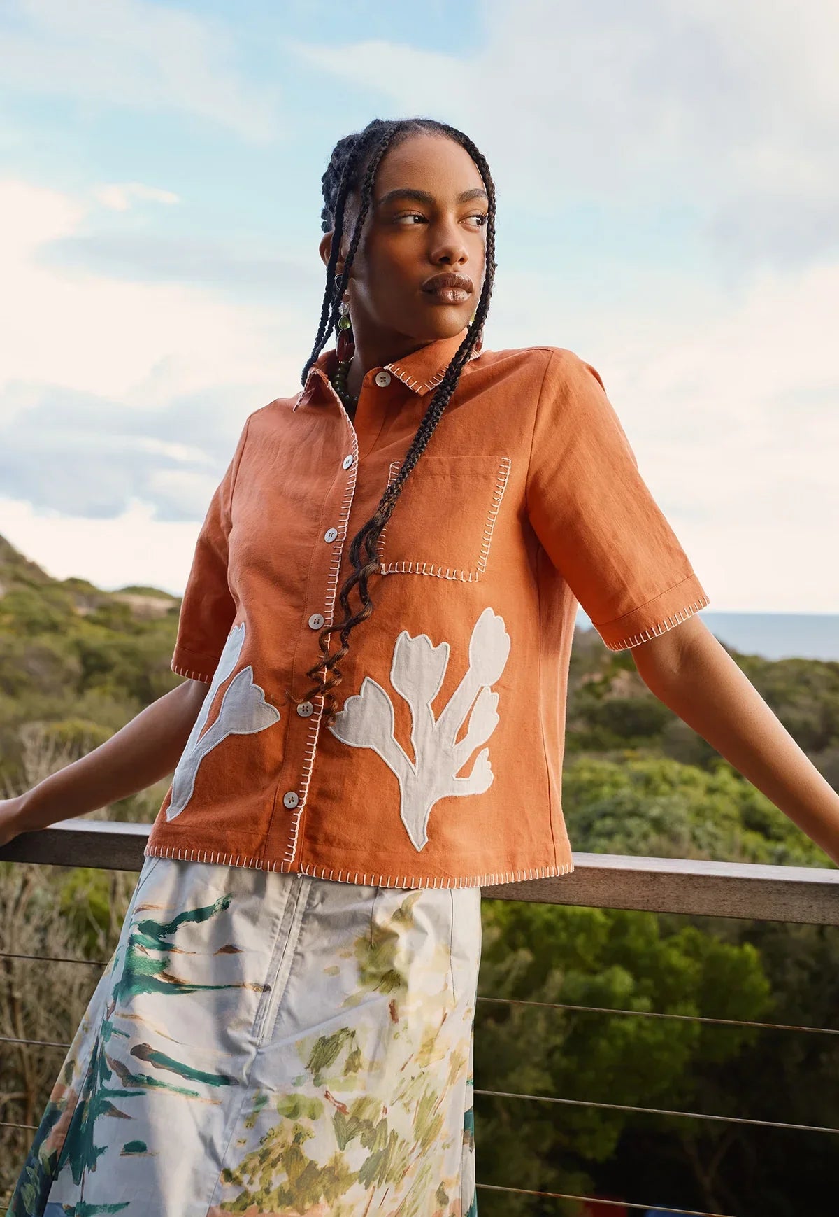 Woman wearing NANCYBIRD Summer Shirt in Blossom Appliqué and a patterned skirt outdoors.