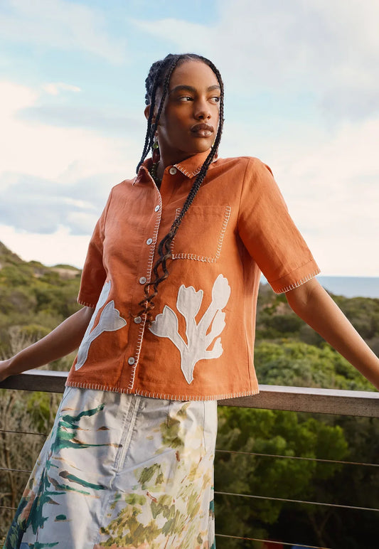 Woman wearing NANCYBIRD Summer Shirt in Blossom Appliqué and a patterned skirt outdoors.