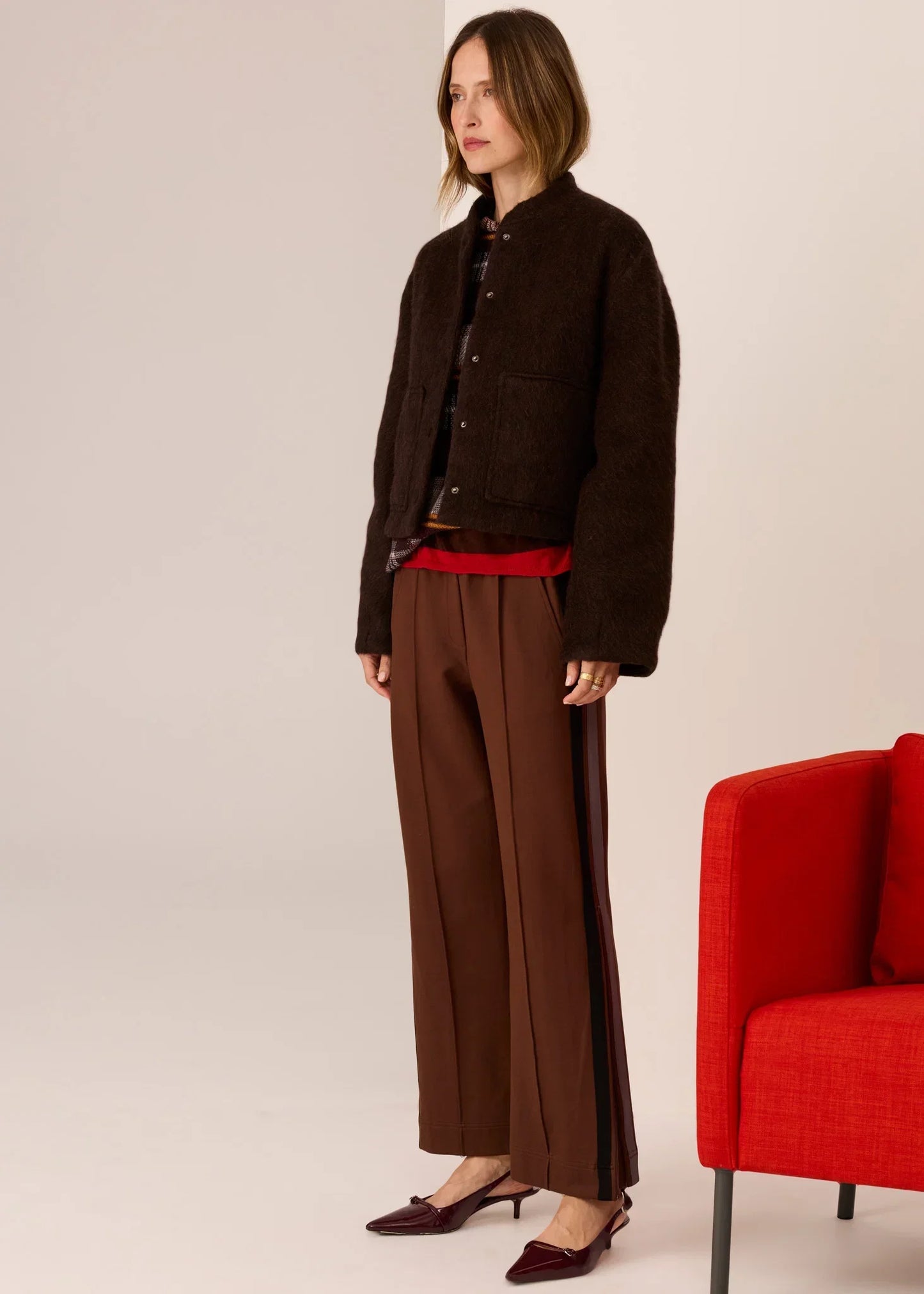 Brown textured jacket with wide-leg trousers and red accents, styled with burgundy heels