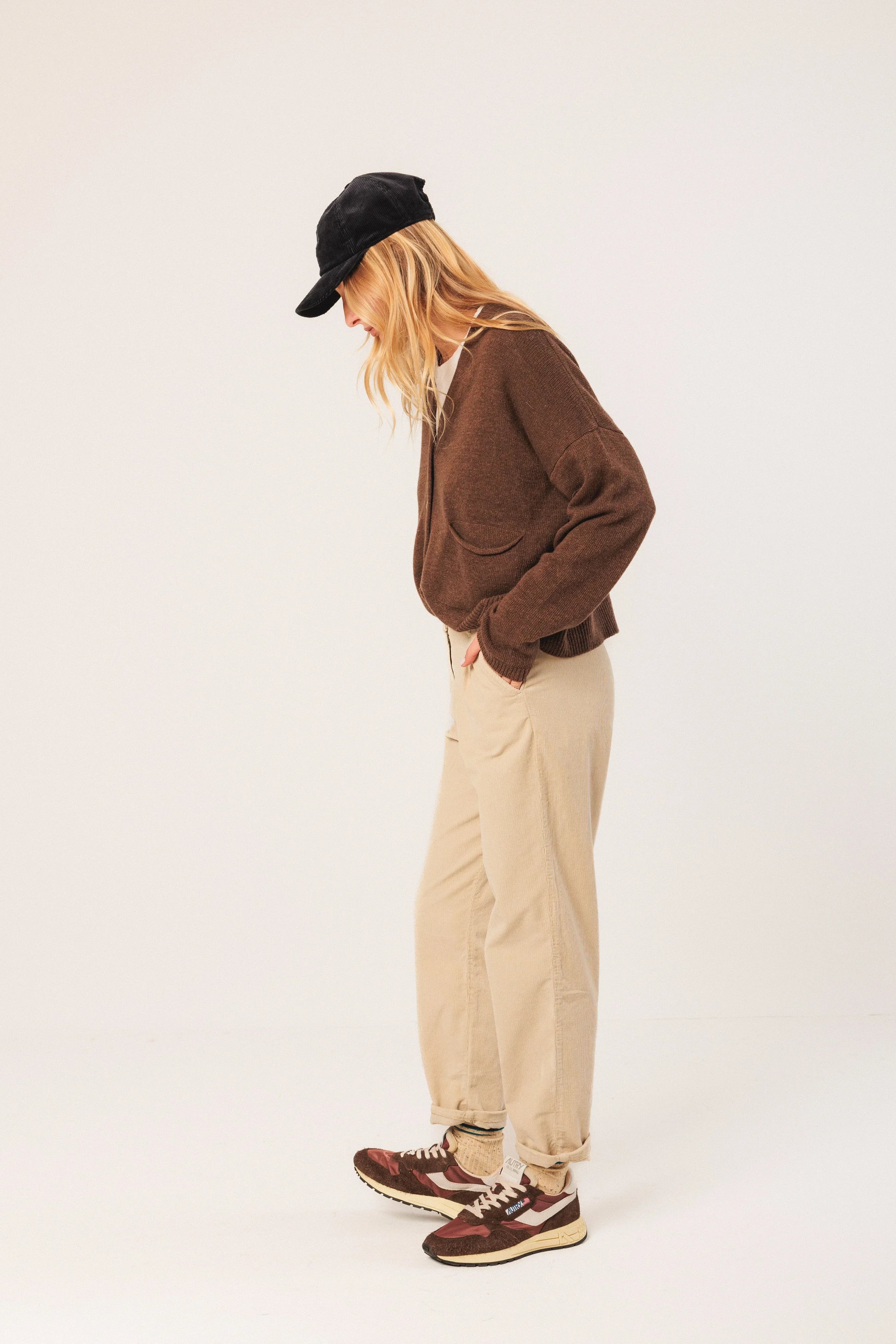 Woman in brown cardigan, beige corduroy pants, and retro sneakers with black cap