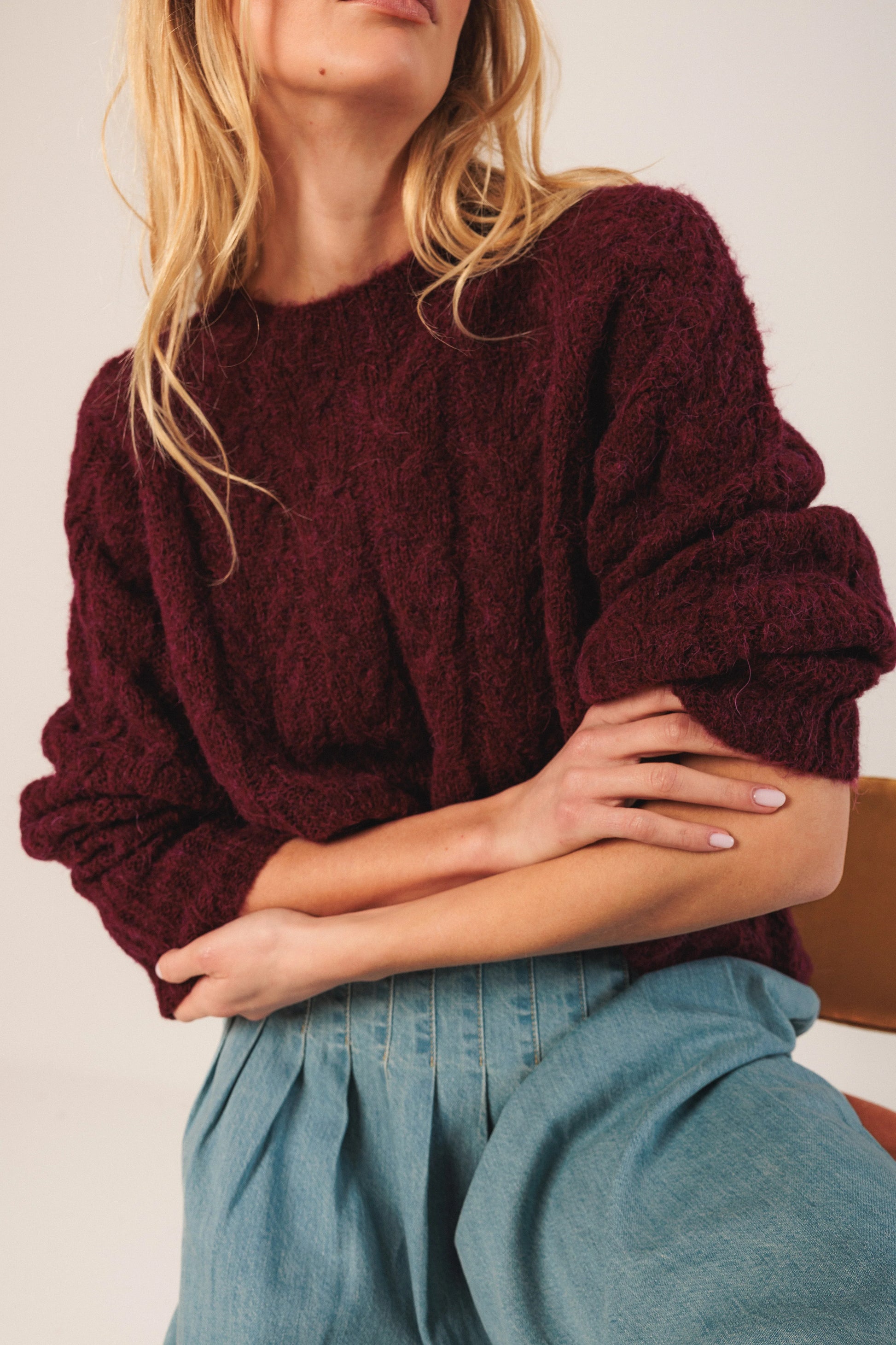 Woman in cozy burgundy knit sweater with puffed sleeves, paired with light blue denim pants.