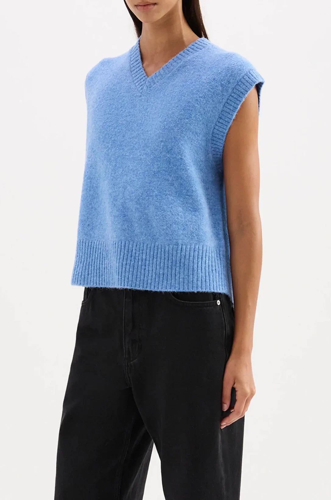 Woman wearing sleeveless blue knit V-neck sweater vest and black high-waisted pants