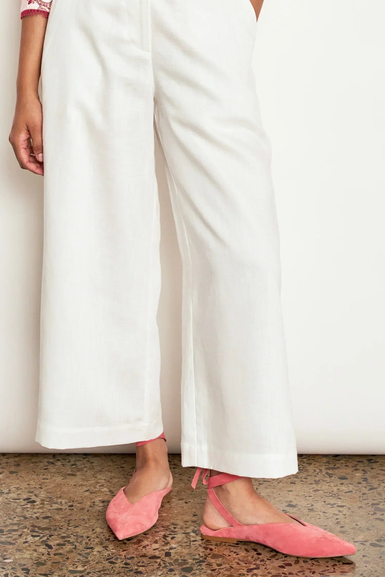 Woman wearing white wide-leg linen trousers and pink suede pointed-toe ballet flats.