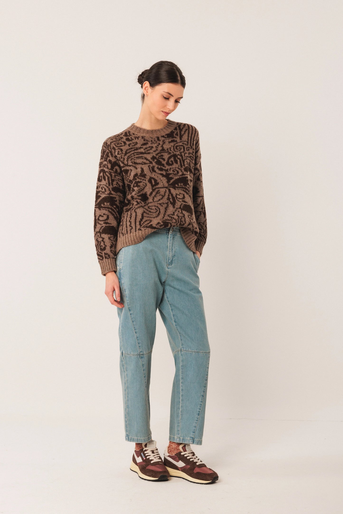 Woman wearing patterned brown sweater, light blue jeans, and retro sneakers for casual fashion