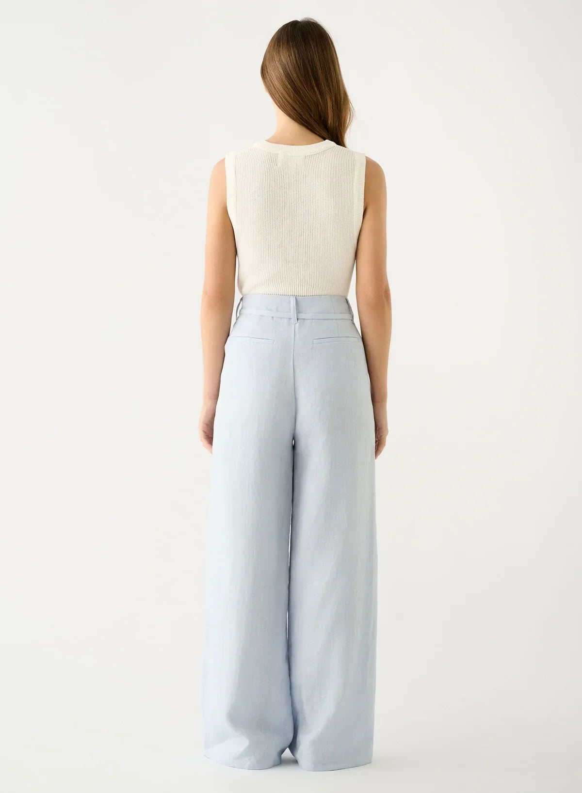 Rear view of a woman wearing a white ribbed top and Esmaee Olivia Pant in ice blue.