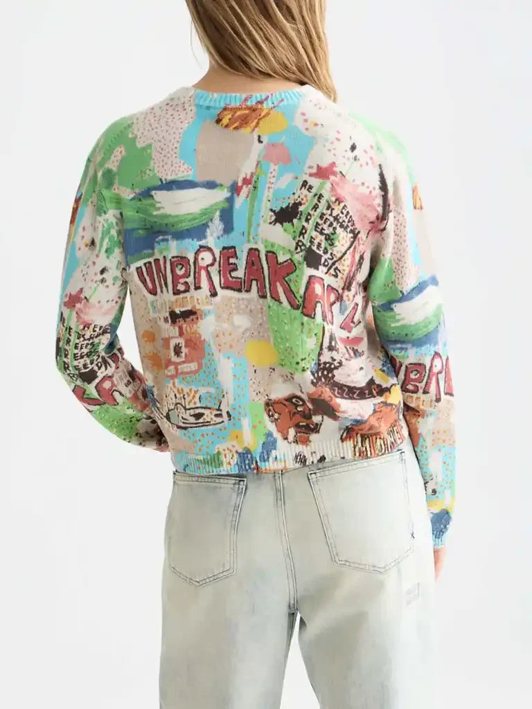 Woman wearing colorful graphic print sweater with 'UNBREAKABLE' text and light wash jeans