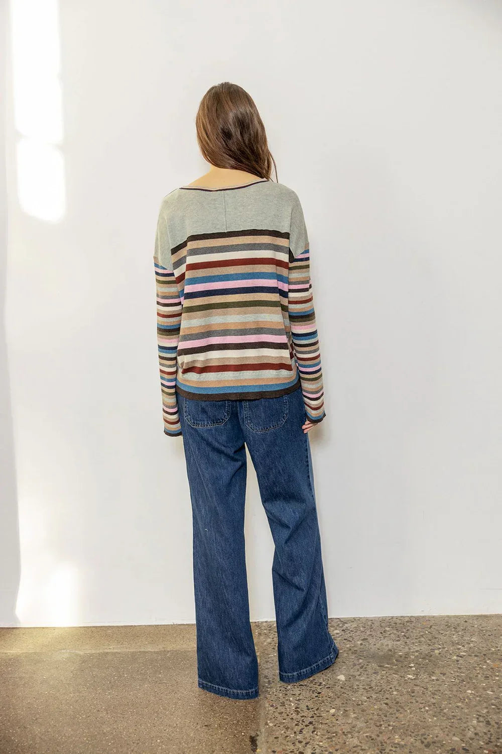 Woman wearing a multicolored striped sweater and wide-leg blue jeans, shown from behind.