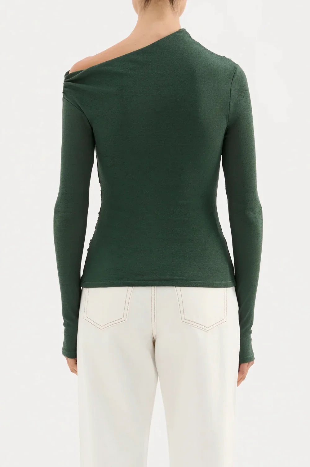 Woman wearing forest green one-shoulder long sleeve top with white high-waisted pants