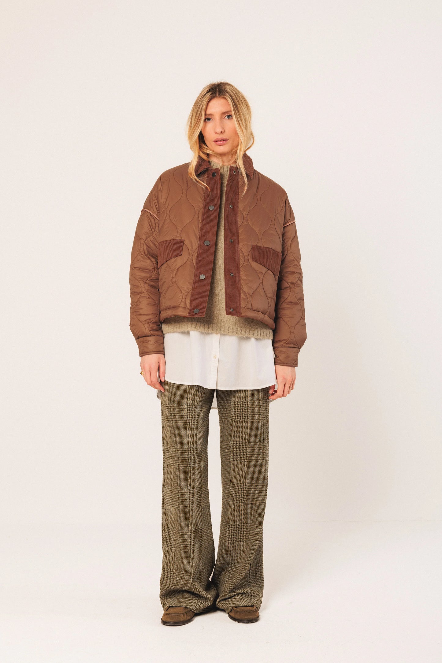 Brown quilted jacket with corduroy trim, layered over sweater and white shirt, paired with green check pants