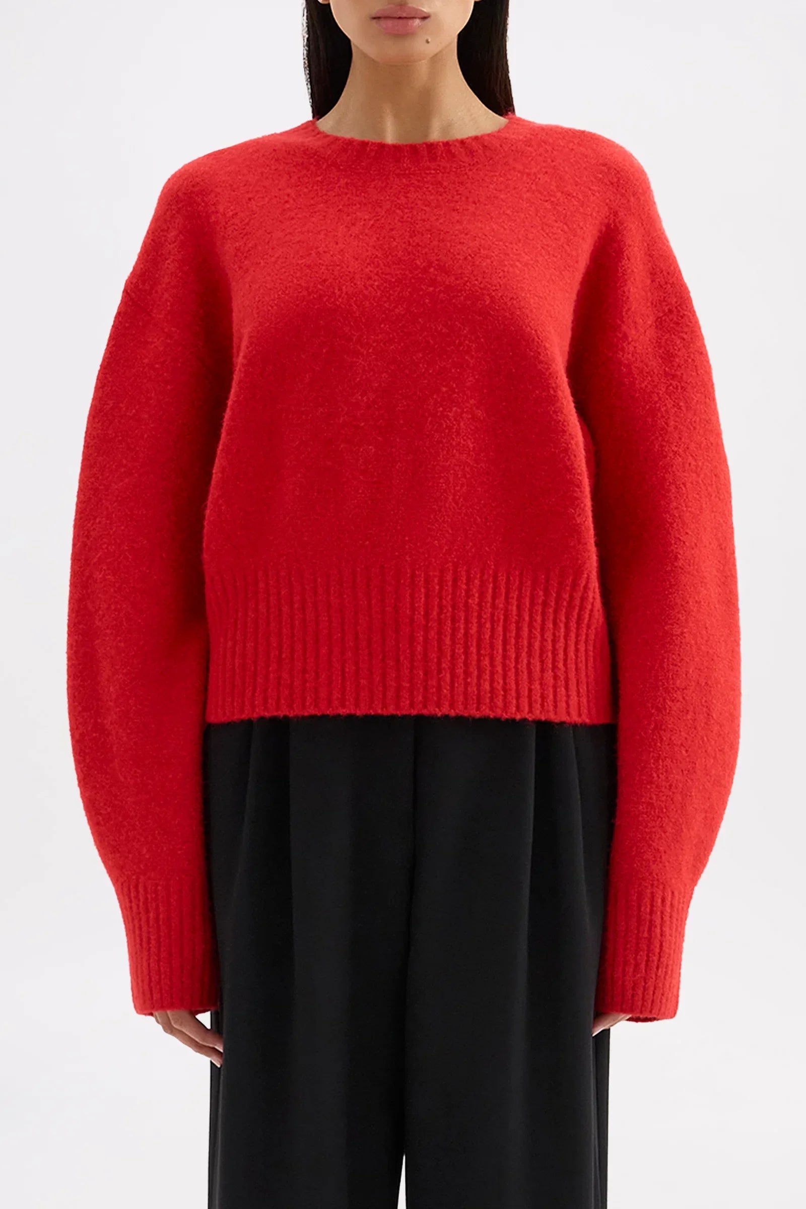 Woman wearing a bright red oversized fuzzy knit sweater and black trousers.