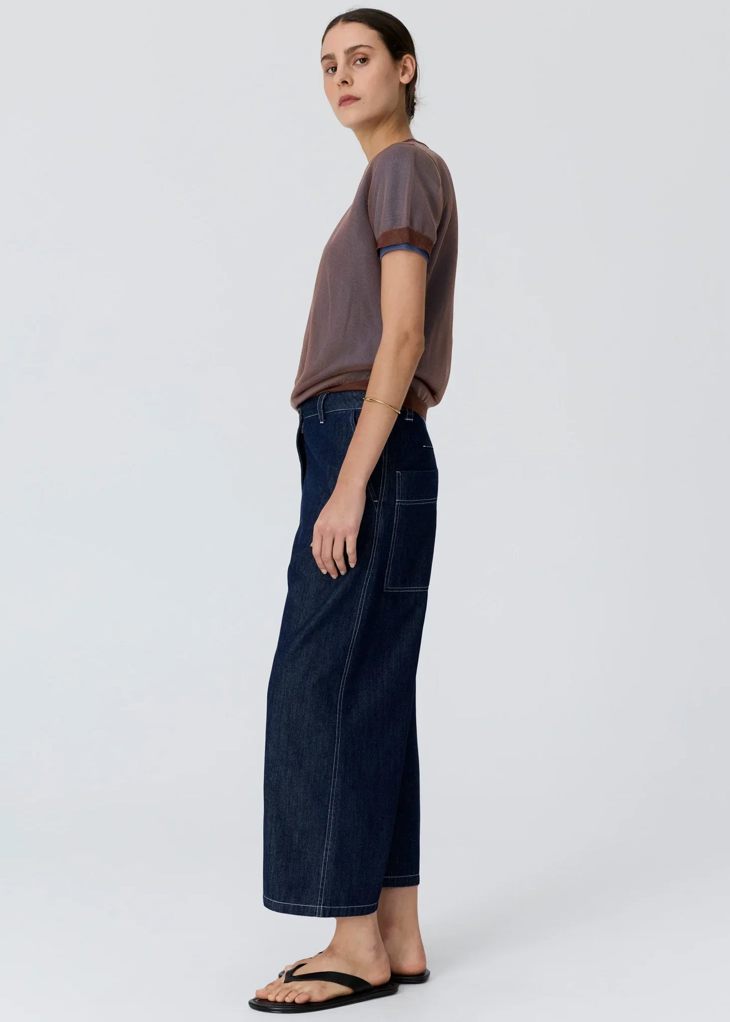 Woman wearing a taupe short-sleeve top and wide-leg dark denim pants with black flip flops.