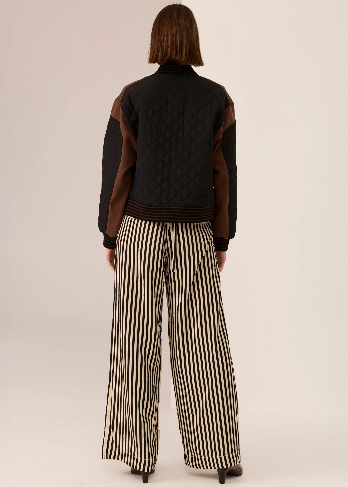 Black quilted jacket with brown sleeves paired with black and cream striped wide-leg pants