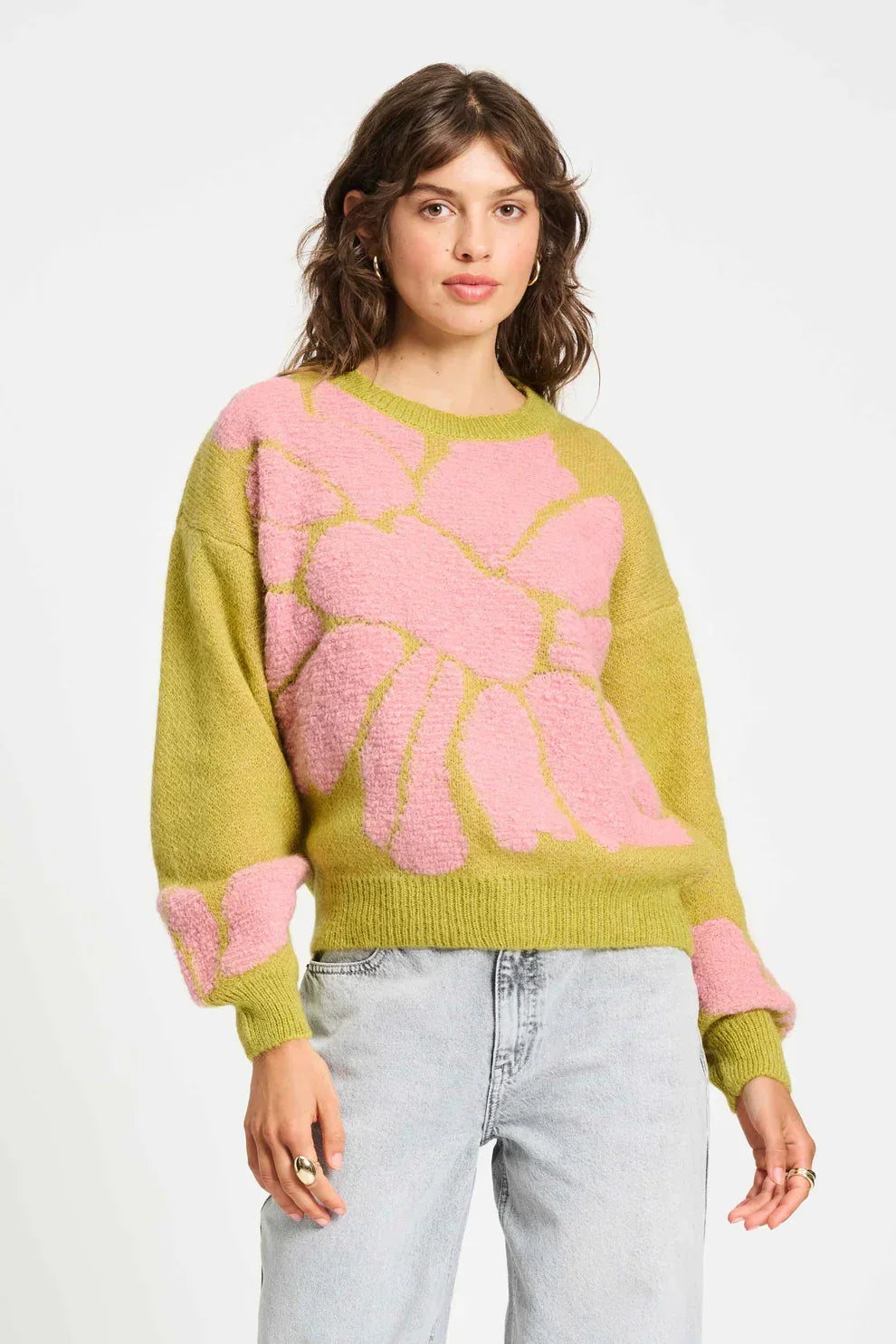 Woman wearing green knit sweater with large pink floral pattern and light wash jeans