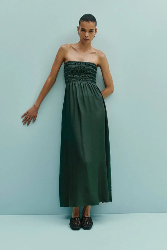 Woman wearing a strapless dark green maxi dress with smocked bodice, black woven flats