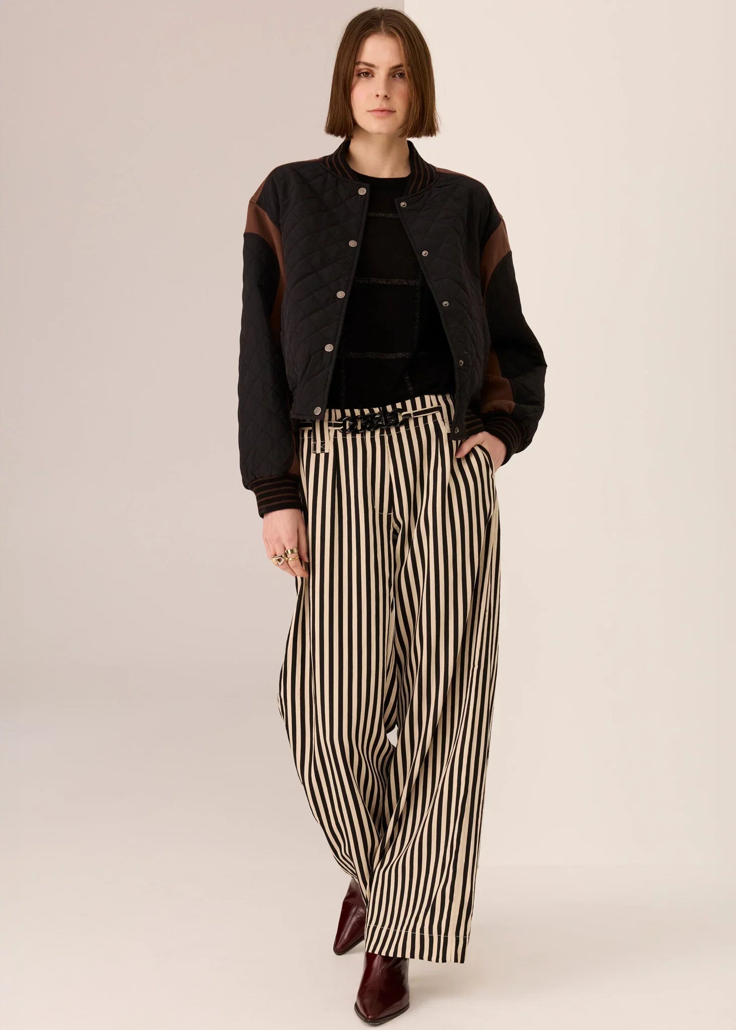 Woman in black quilted jacket, striped pants, and burgundy boots for stylish women's fashion