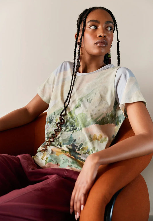Woman wearing a NANCYBIRD Apollo Tee in Mountain Peak with a scenic landscape print.