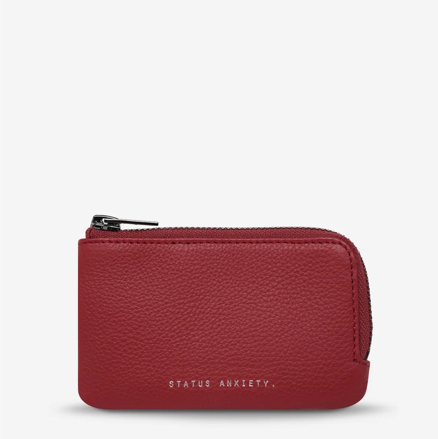 Red pebbled leather zip coin purse with 'STATUS ANXIETY.' branding, minimalist design for everyday carry.