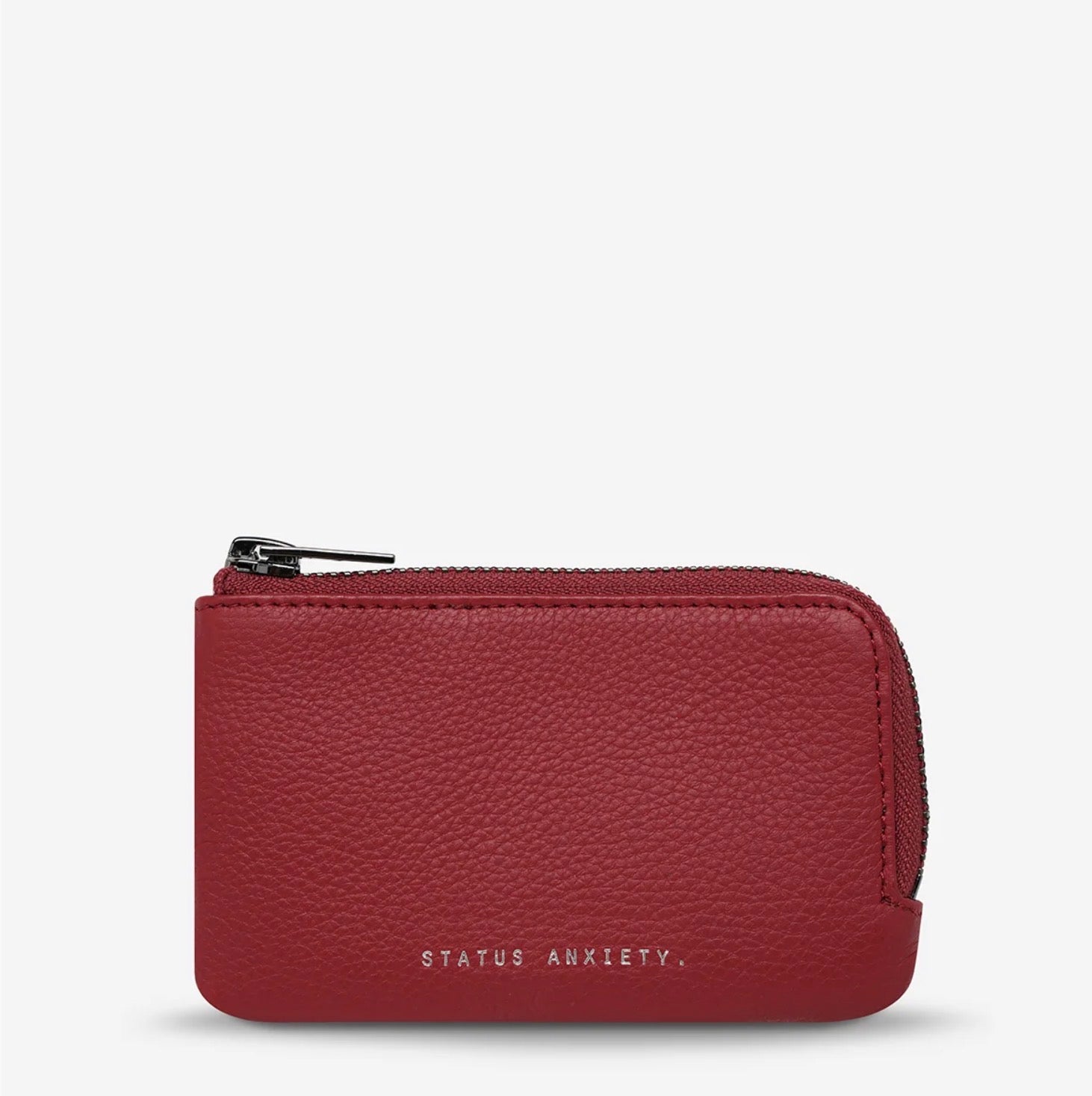 Red pebbled leather zip coin purse with 'STATUS ANXIETY.' branding, minimalist design for everyday carry.