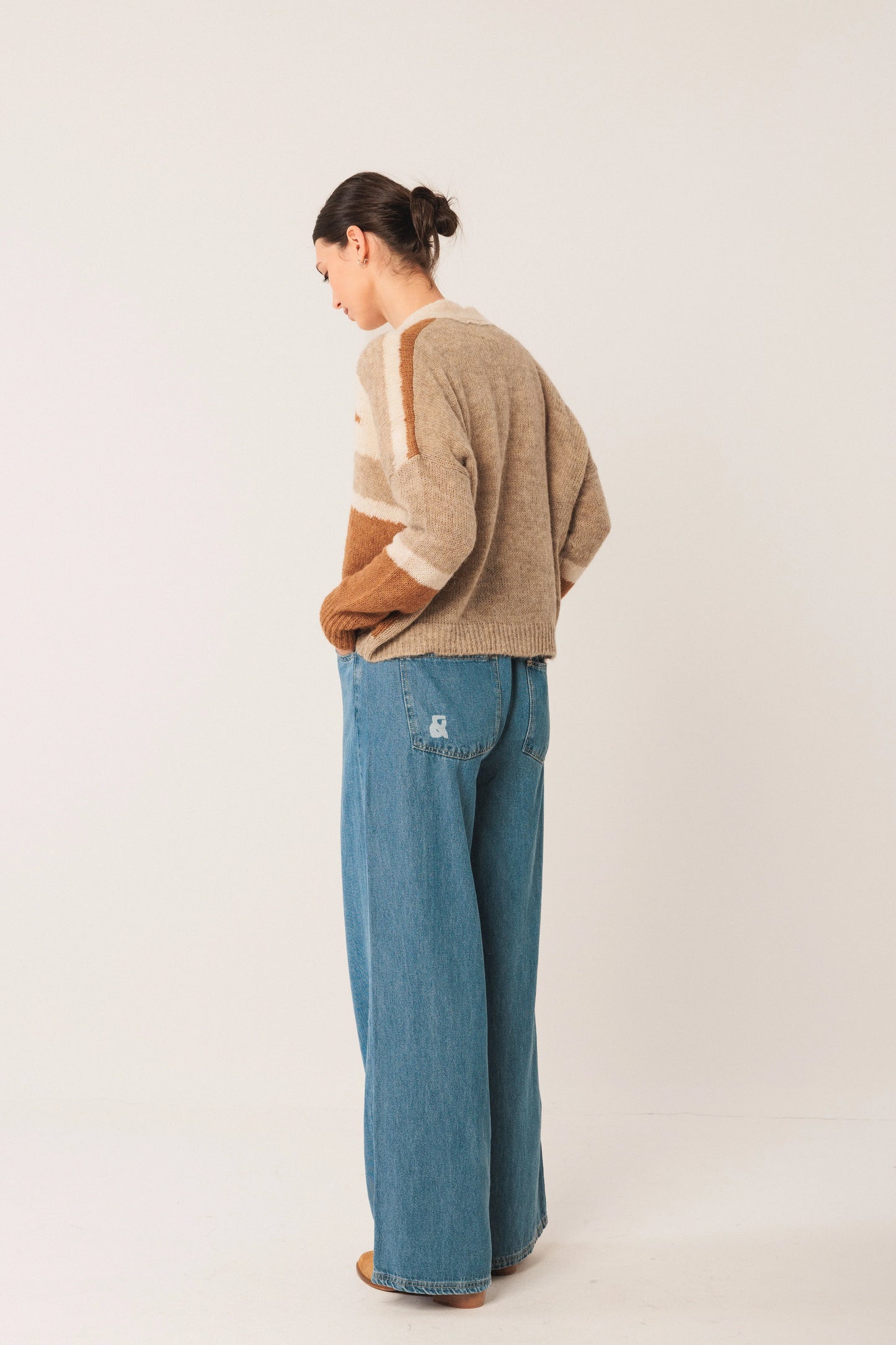 Woman in beige and brown striped knit cardigan with wide-leg blue jeans, side view