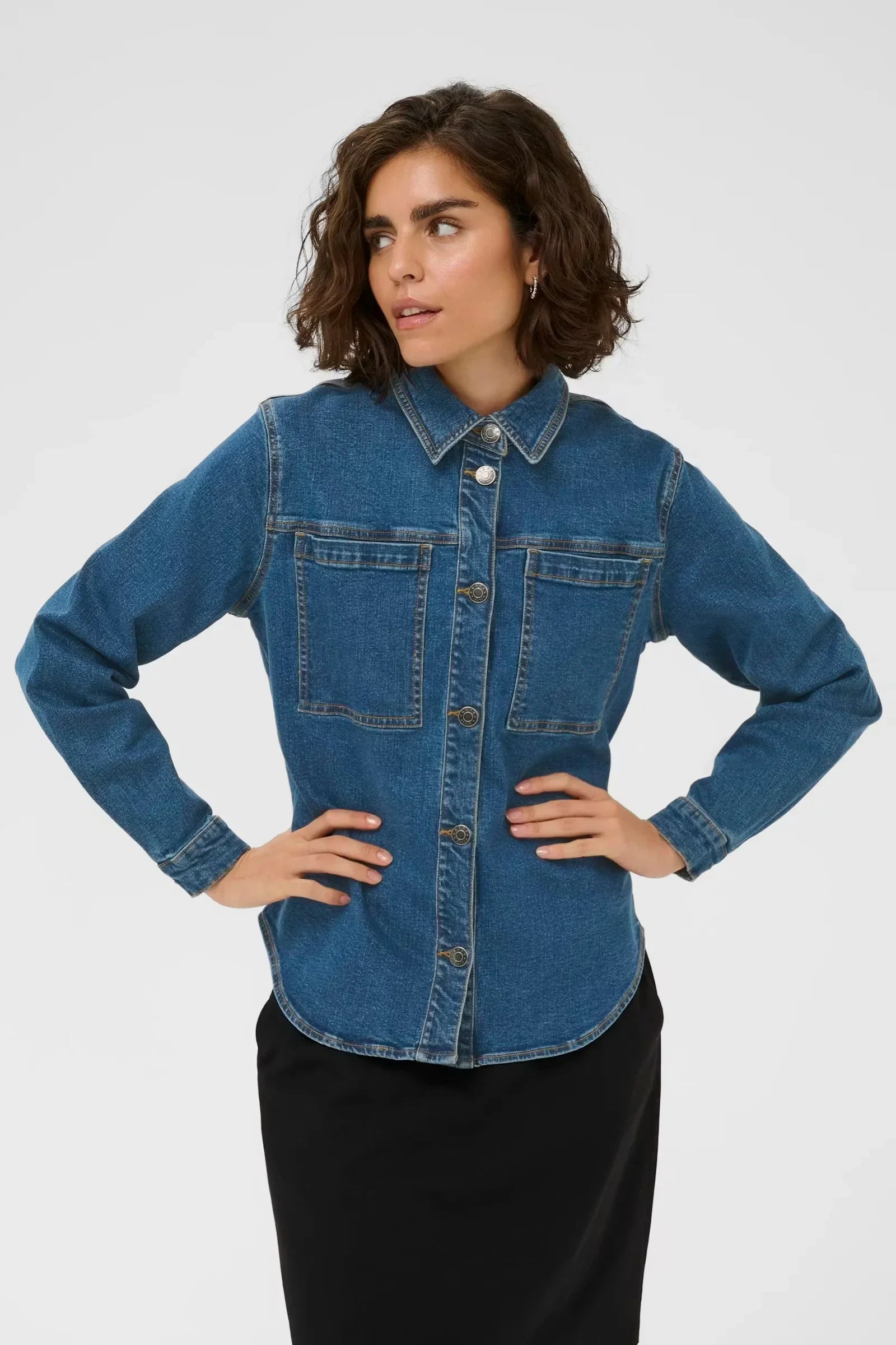 Woman modeling blue denim shirt with button front and chest pockets, styled with black skirt