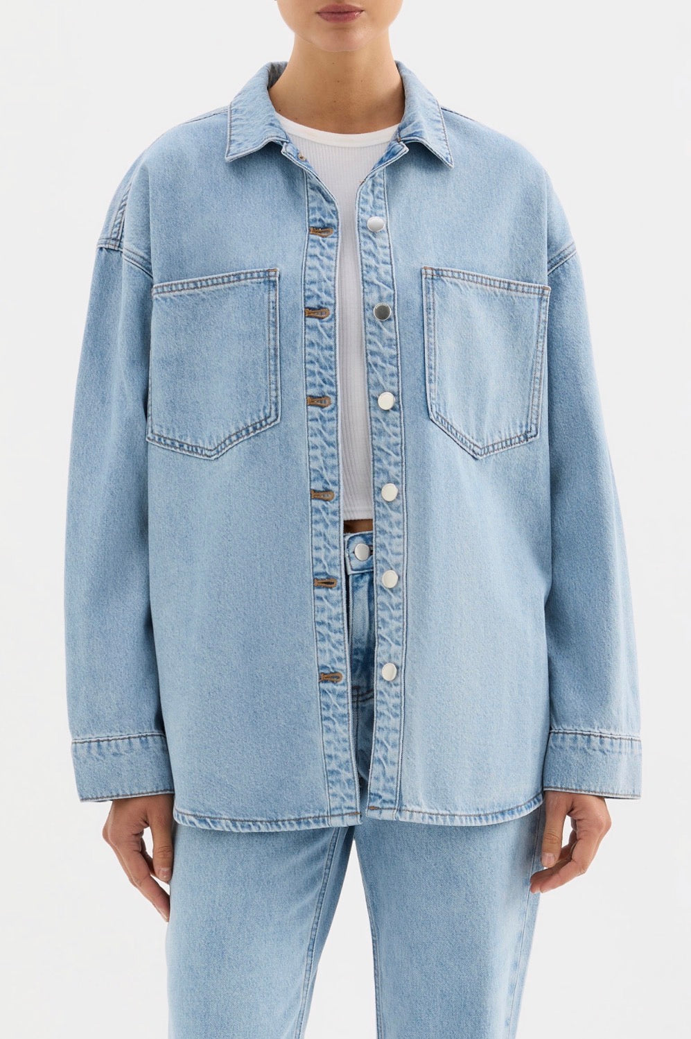 Light blue denim shirt with front pockets and button closure, paired with matching jeans