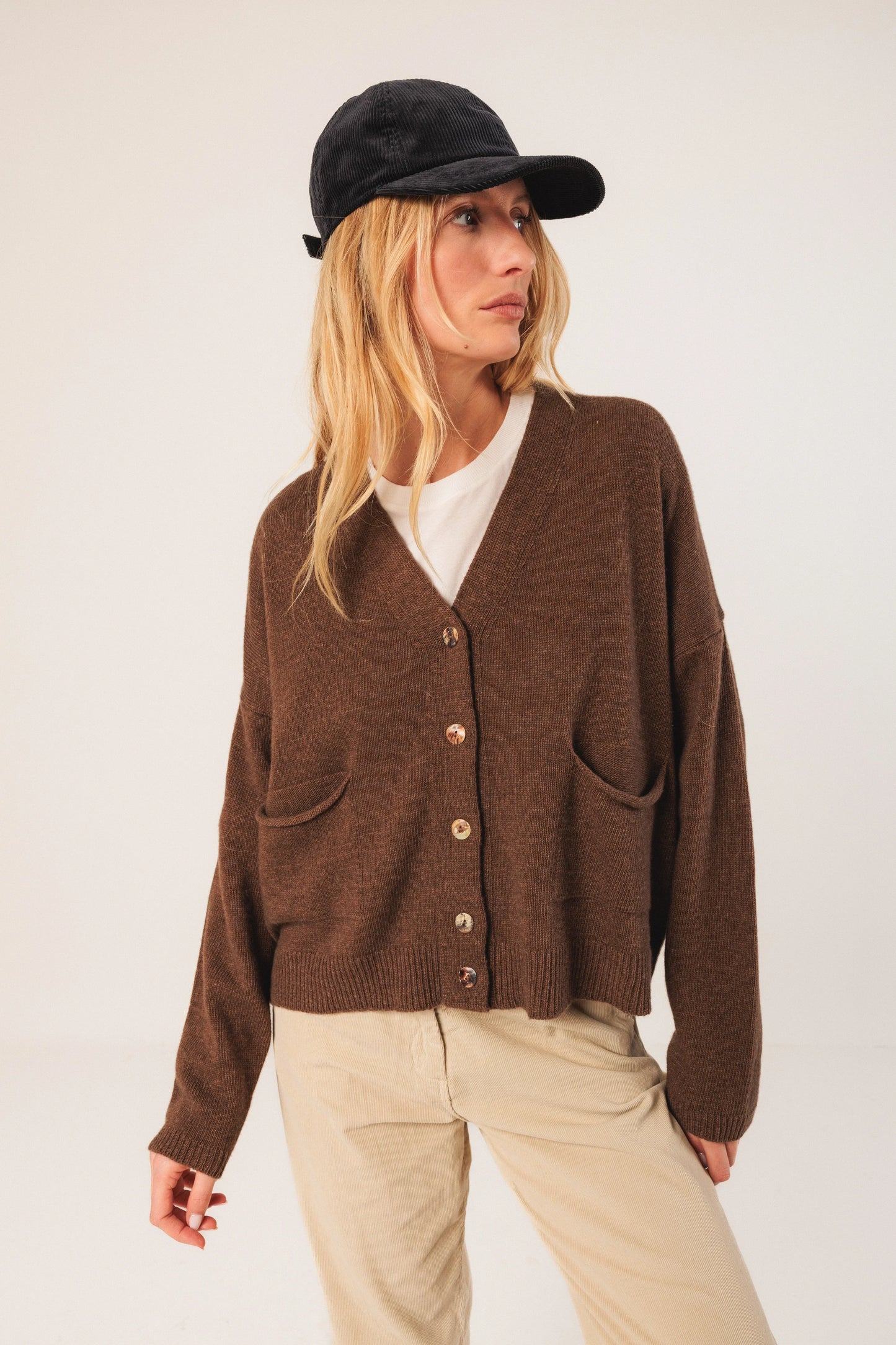 Brown knit cardigan with buttons, paired with beige pants and black cap for casual women's fashion