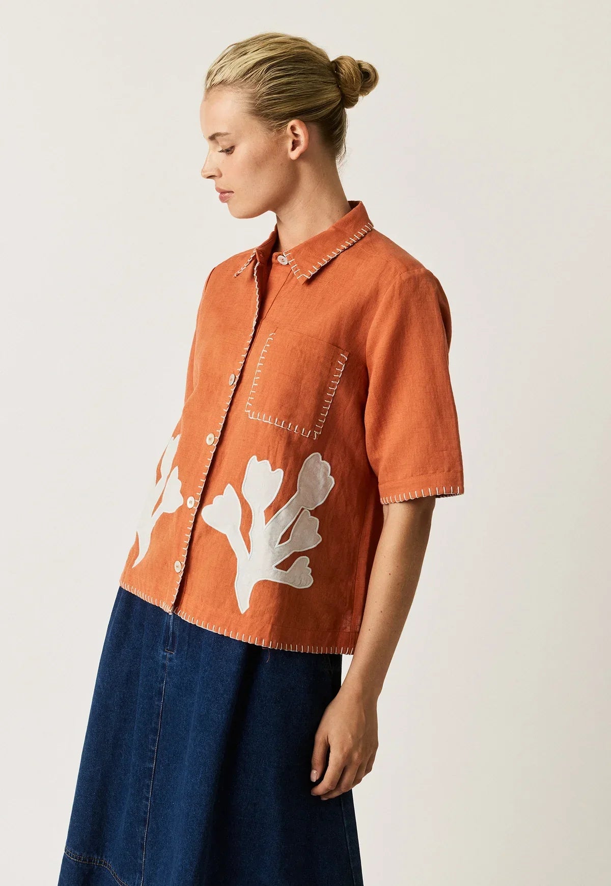 Woman wearing NANCYBIRD Summer Shirt in Blossom Appliqué in orange with white floral details.