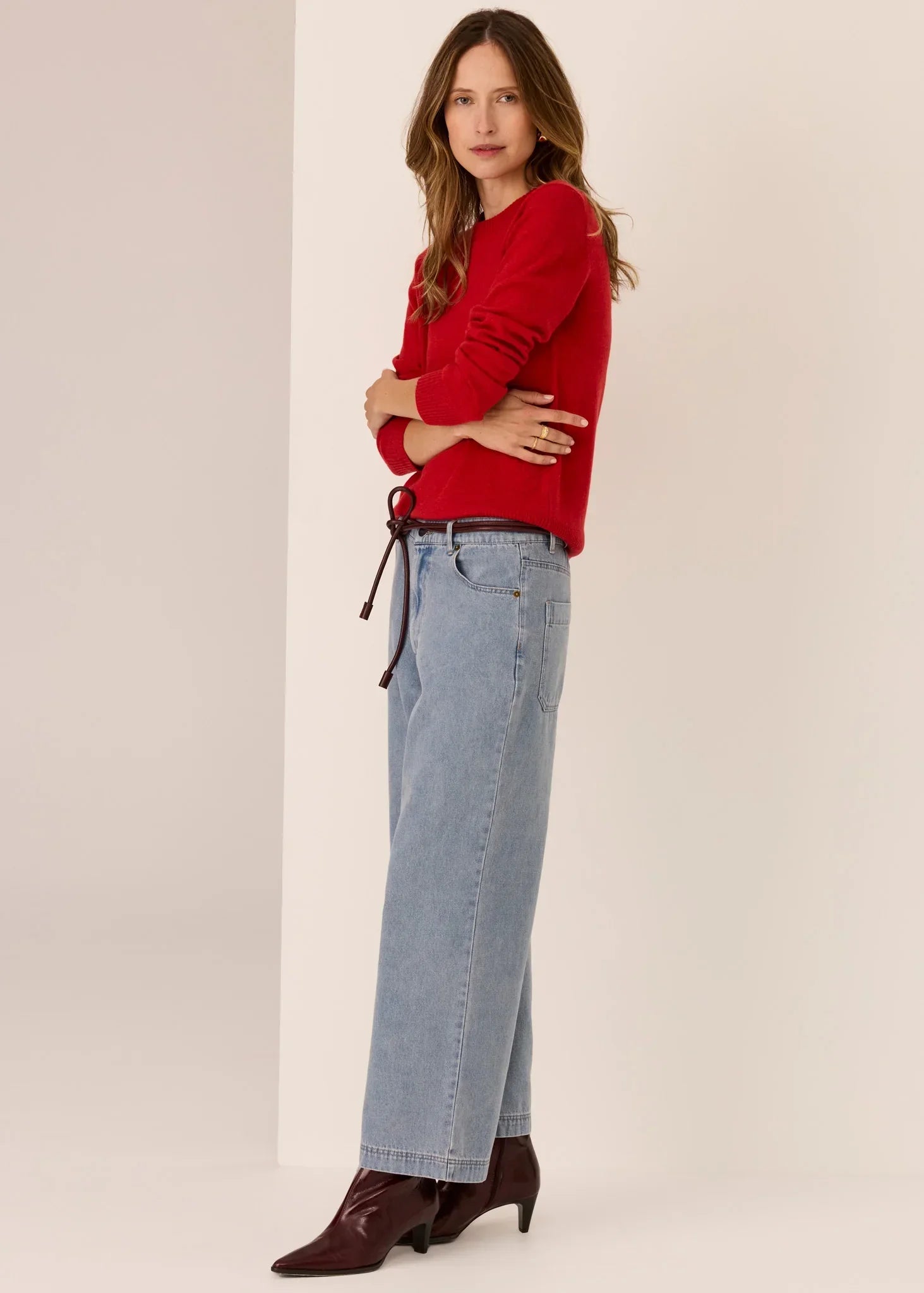 Woman in red sweater, light blue wide-leg jeans, and brown ankle boots, standing sideways