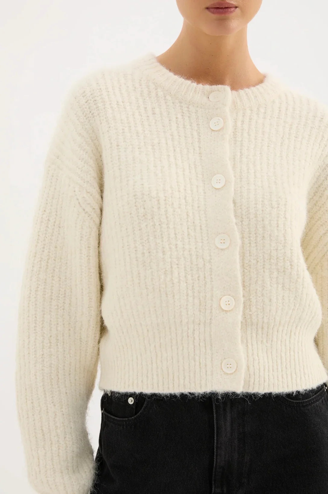 Woman wearing a cream textured knit button-up cardigan and black jeans