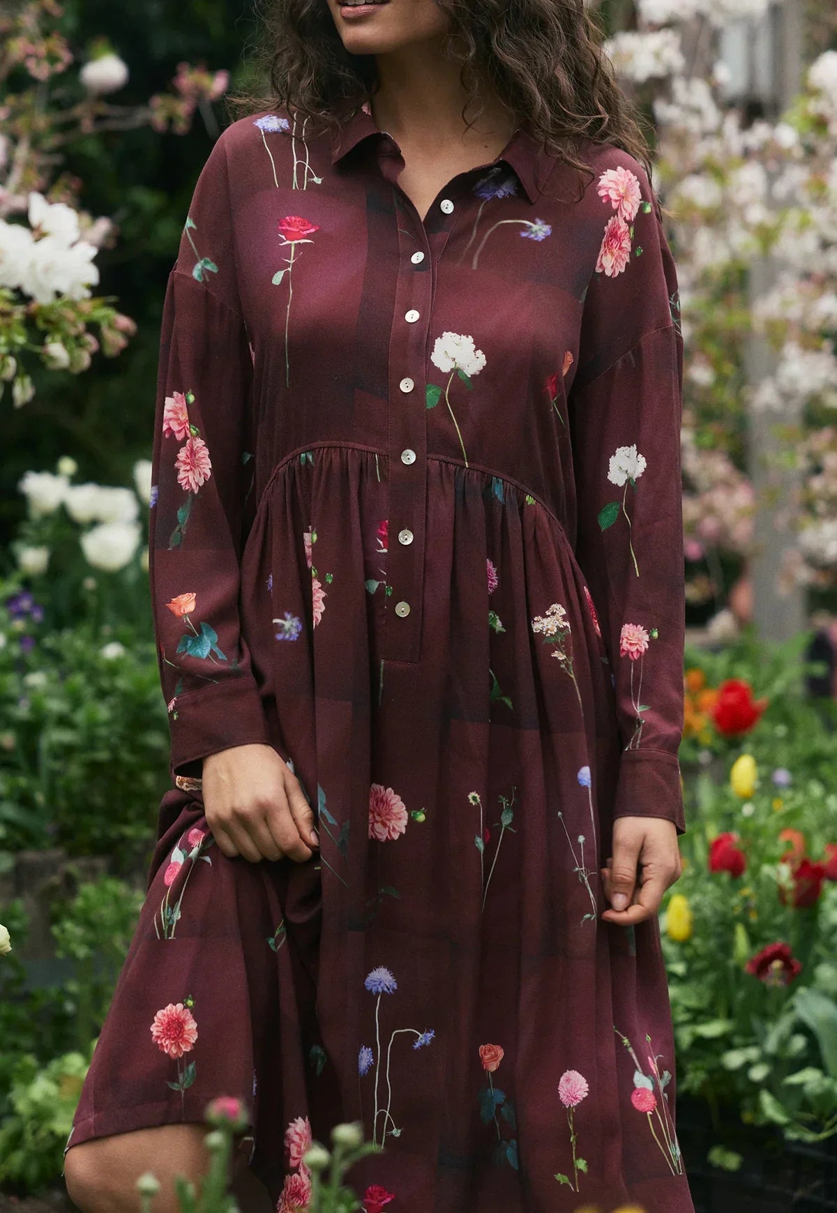Burgundy floral print shirt dress with button front, long sleeves, and flared skirt in garden setting