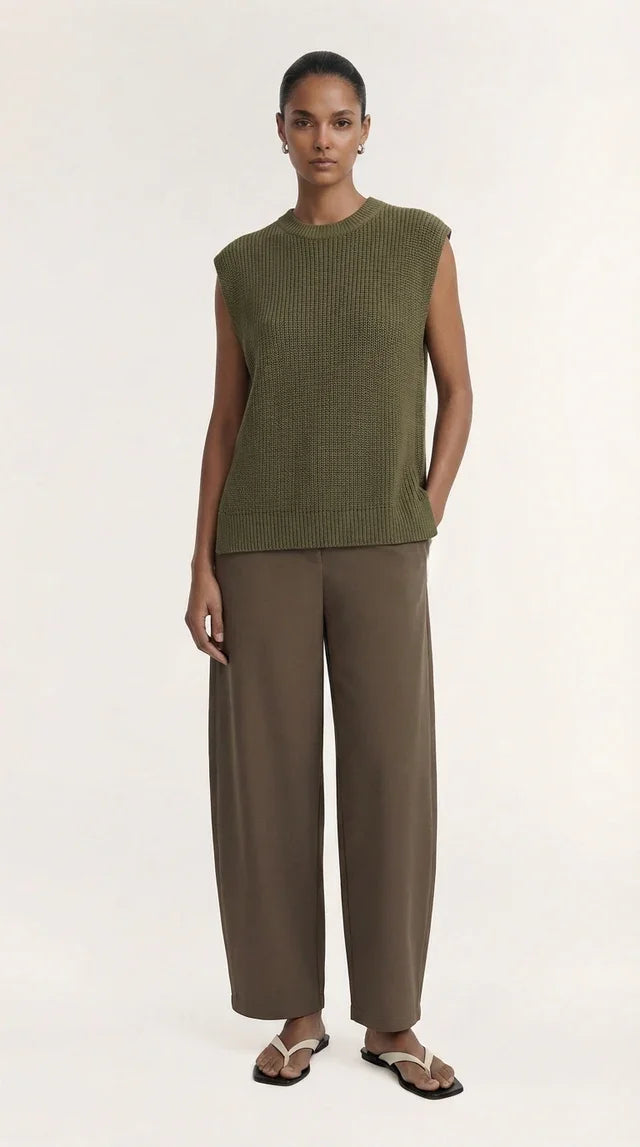 Woman wearing an olive green sleeveless knit top and brown wide-leg trousers with sandals.