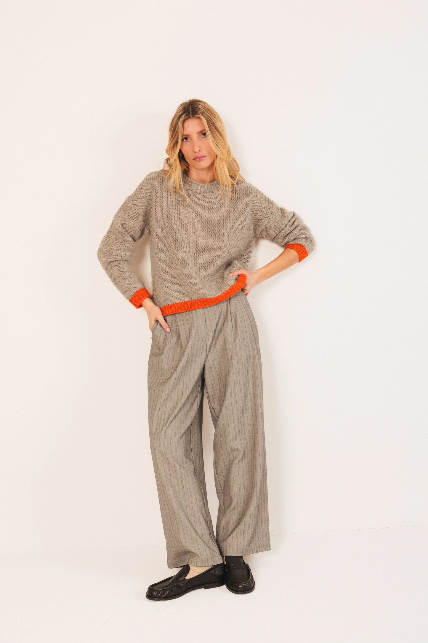 Woman in beige knit sweater with orange trim, wide-leg trousers, and black loafers