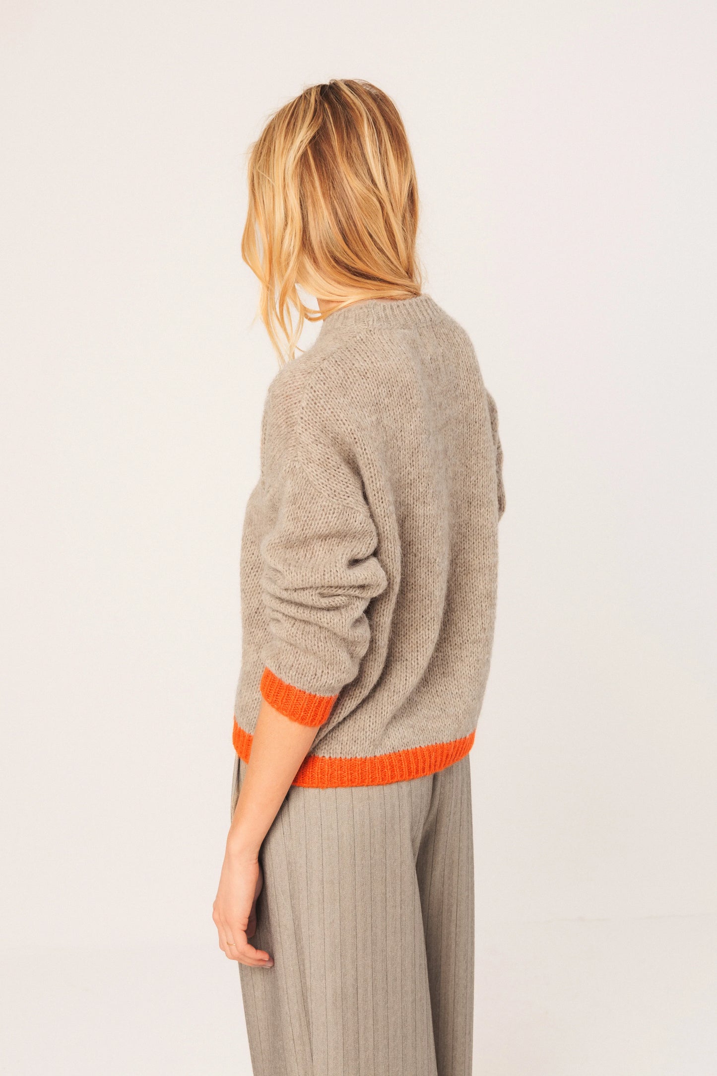 Beige knit sweater with orange trim, back view, paired with grey pinstripe pants for women's fashion