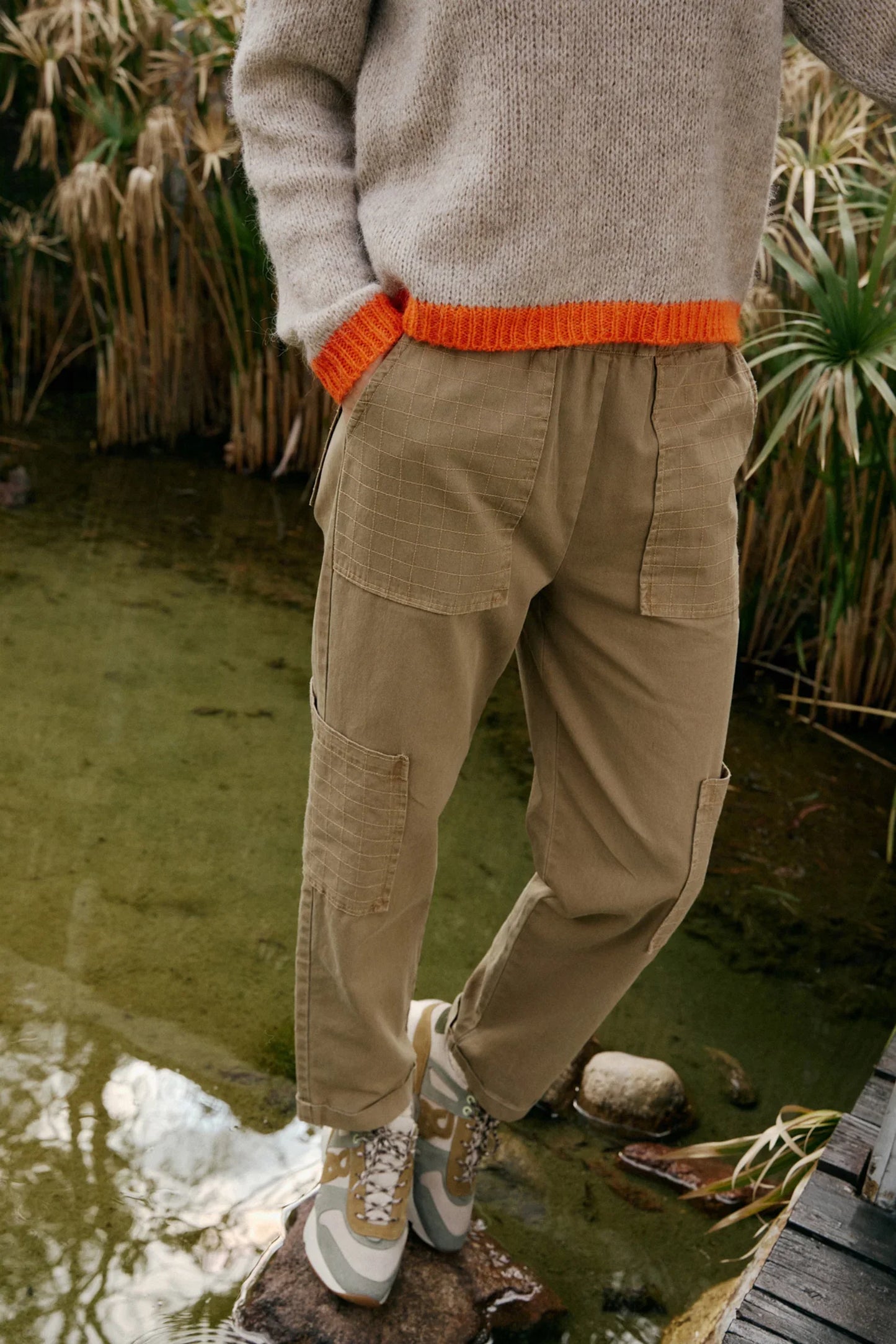 Beige cargo pants with grid pockets, paired with a cozy knit sweater and sneakers, styled for casual outdoor wear.