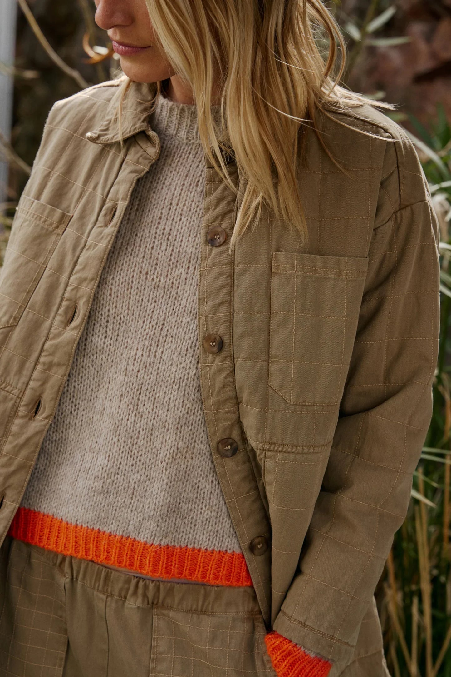 Beige quilted jacket with button front over cream knit sweater with orange hem, styled with matching pants