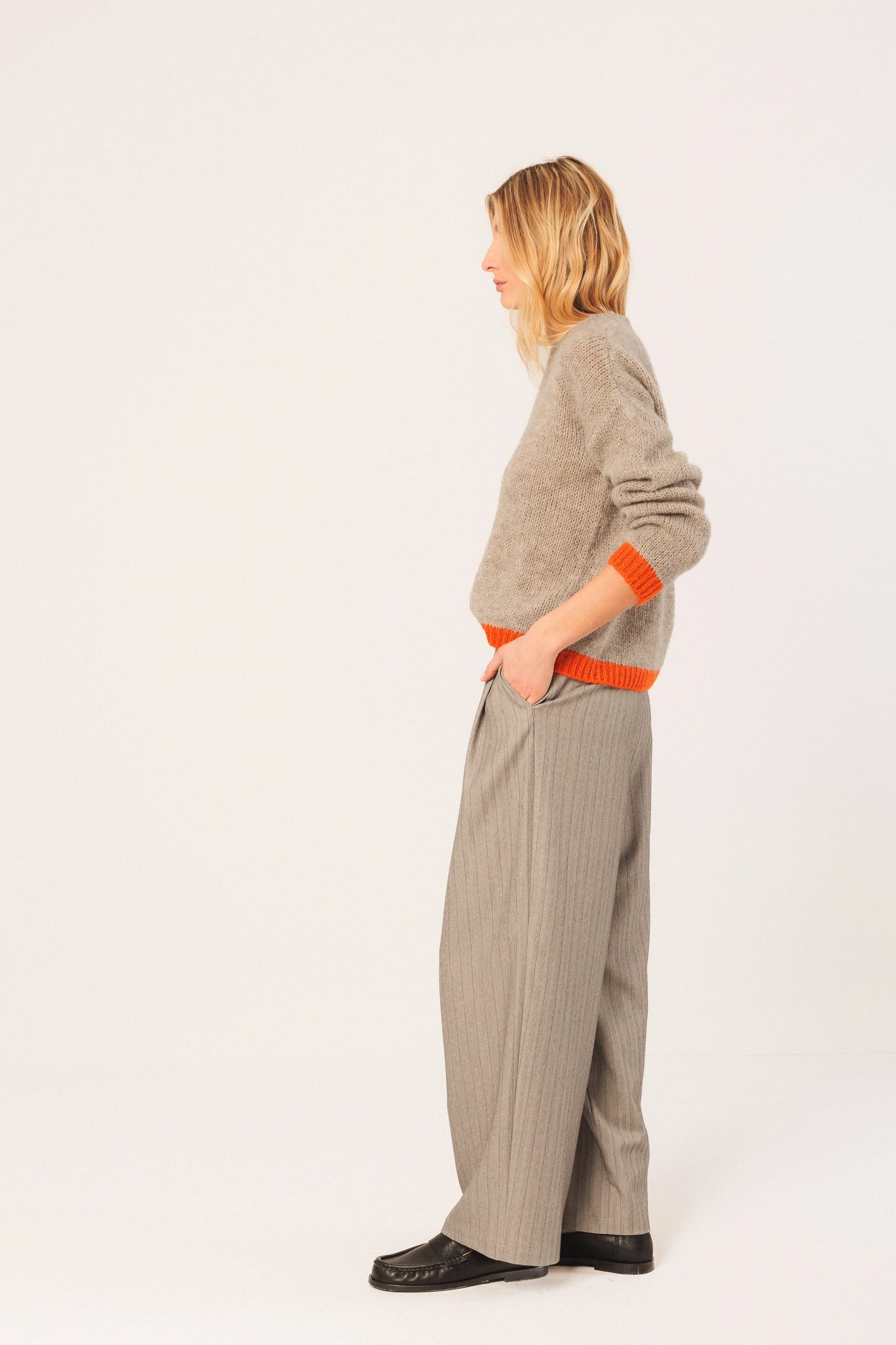 Woman in beige knit sweater with orange trim, wide-leg pinstripe pants, and black loafers