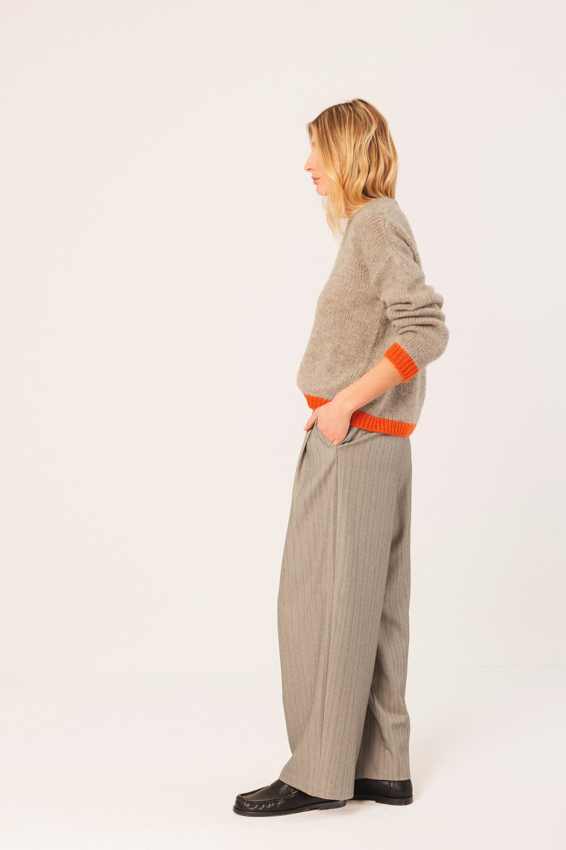 Woman in beige knit sweater with orange trim, wide-leg pinstripe pants, and black loafers